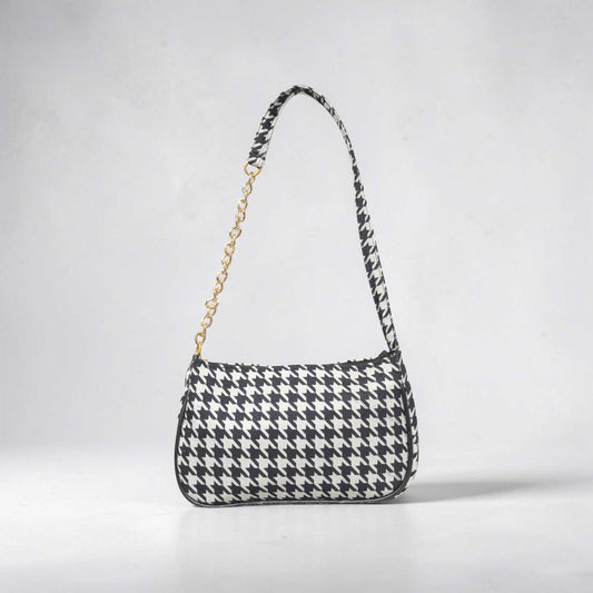 Black and white houndstooth patterned handbag with a gold chain on a light gray background